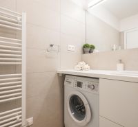 A bathroom with light tiles, a washing machine, a sink, and towels in a 2-room apartment.