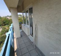 The balcony of a 2-room apartment with blue railings and a view of greenery in Bratislava.