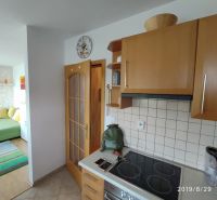 A kitchen in a 2-room apartment with wooden cabinets and a view of the living room.
