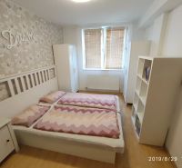 A bedroom with a bed, wooden decor flooring, and floral wallpaper in a two-room apartment.
