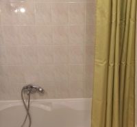 Bathroom with white tiles and a bathtub with a curtain in a 2-room apartment.