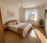 A bright bedroom with a bed, wooden floor decor, and plants in a 3-room apartment.
