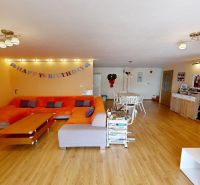 Living room with an orange sofa, dining table, and wood-patterned flooring.