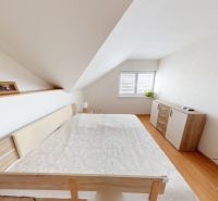 A bedroom in a family house with a wooden decor floor and a slanted ceiling.