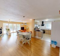 Bright living room with wood-patterned flooring and a kitchen in a family house.