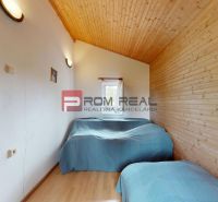 The interior of a cabin with beds, a wooden decor floor, white walls, wooden ceiling.