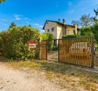 The cottage at Alžbeta's court in Miloslavov surrounded by greenery and a wooden fence.