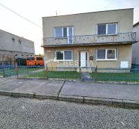 A family house in Senica with a balcony, a blue fence, and a parked car.