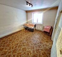 A room in a family house with a wooden decor floor, white walls, and a window.
