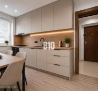 A bright kitchen with wood-patterned flooring and a simple table in a three-room apartment.