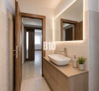 A bathroom in a 3-room apartment with a sink and a backlit mirror on the wall.