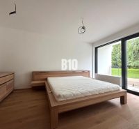 Bedroom with a bed and a dresser, wooden decor flooring, large window facing the garden.