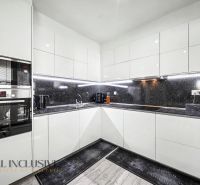 The kitchen of a 3-room apartment with white cabinets and a black countertop.
