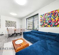 Living room of a three-room apartment with colorful paintings, a blue sofa, and a dining table.