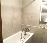 A bathroom with a bathtub and light tiles in a 2-room apartment.