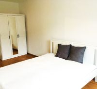 Bedroom in a 2-room apartment with a white bed and wardrobe on a wooden floor.