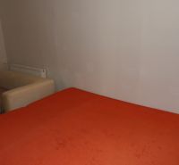 A room with an orange bed and a beige armchair in a 2-room apartment.