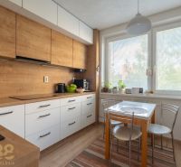 A kitchen with a wooden decor floor in a 3-room apartment, with a dining table by the window.