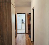 A hallway in a family house with a wooden decor floor and a view into the kitchen.