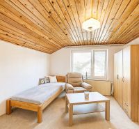 Interior of a family house with a wooden ceiling, an armchair, and a bed next to the window.