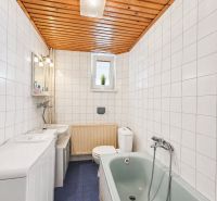 Bathroom with tiles, blue floor, bathtub, and wooden ceiling in a family house.