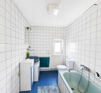 A bathroom with a shower and a bathtub tiled with white tiles in a family house.