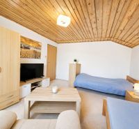 A room in a family house with a wooden ceiling, beds, and a TV.