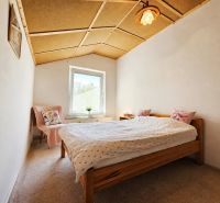 Bedroom in a family house with a wooden ceiling, carpet, and a bed with pillows.
