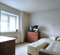 A room with a couch, table, wooden decor, TV, and a window with blinds.