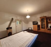 A bedroom in a family house with a dark floor, furniture, a television, and a stove.