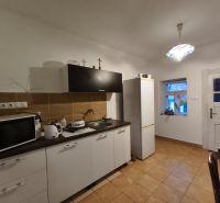 A kitchen in a family house with brown tiles, equipped with a microwave and a refrigerator.