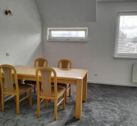 A table with four chairs in a two-room apartment, gray carpet, two windows.