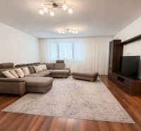 Living room with a large sofa, television, and wooden decor flooring in a family house.