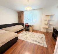 Two beds, a desk, and a shelf in a room of a family house with a wood-patterned floor.