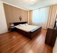 Bedroom in a family house with a bed, curtains, and a wood-patterned floor.