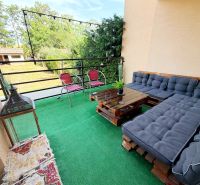 A balcony of a family house with pallet seating, a green carpet, and a view of the garden.
