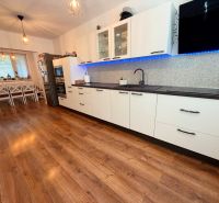 A kitchen with a wood-patterned floor, white cabinets, and a dining table in a family house.
