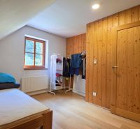 Part of a bedroom in a cabin with a single bed, window, and coat rack, floor with wooden decor.