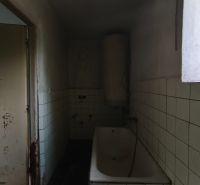 A bathroom with a bathtub and tiles in a family house. Damage is visible on the wall.