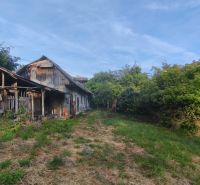 An older family house in Čelovce surrounded by greenery, lawn, and blue sky.
