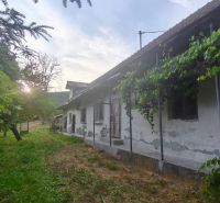 An older family house in Čelovce surrounded by greenery with a sunset in the background.
