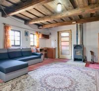 Living room in a family house with a wooden ceiling, sofa, and tiled stove.