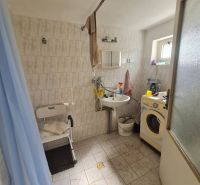 A bathroom in a family house with a washing machine, shower, and small window.