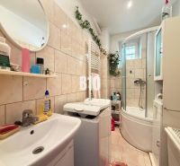 A bathroom in a family house with a washing machine, bathtub, sink, and a shelf with products.