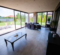 A glazed terrace of a family house with a view of the garden and a tiled floor.