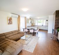 Living room in a family house with a kitchen, beige sofa, and wooden decor flooring.