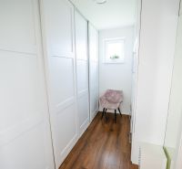 A narrow hallway in a family house with a wood-patterned floor and a window.