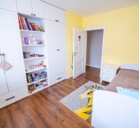 A children's room in a family house with a white wardrobe, a brown bed, and a wooden-patterned floor.