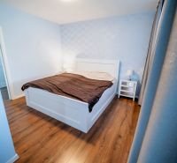 A bedroom in a family house with a bed, nightstands, and a floor with a wood decor.