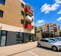 Commercial premises on Okružná Street in Stupava, parking lot with cars, balconies, and a café.